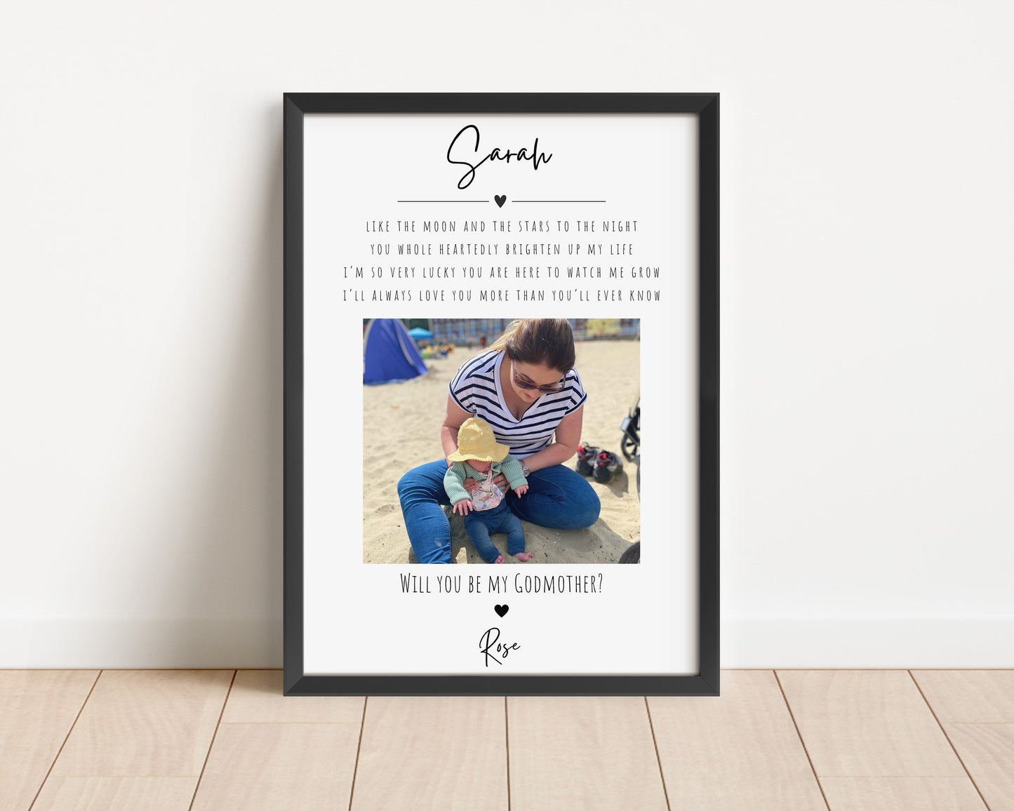 A framed print featuring a photo, surrounded by a heartfelt design. Above the photo is a touching quote:
"Like the moon and the stars to the night, you wholeheartedly brighten up my life. I’m so very lucky you are here to watch me grow. I’ll always love you more than you’ll ever know."
Below the photo is the question, "Will you be my Godmother?" followed by a name in script. The print is set in a wooden frame, styled with neutral, modern decor, creating a warm and sentimental display.