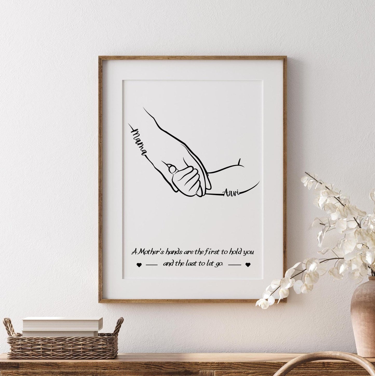 A line art illustration featuring a pair of hands, one labeled &quot;Mum, Mummy, Muma etc&quot; and the other labeled with the name of a child. The hands are gently holding each other, symbolizing love and care. Below the hands, a quote reads: &quot;A Mother’s hands are the first to hold you and the last to let go.&quot;